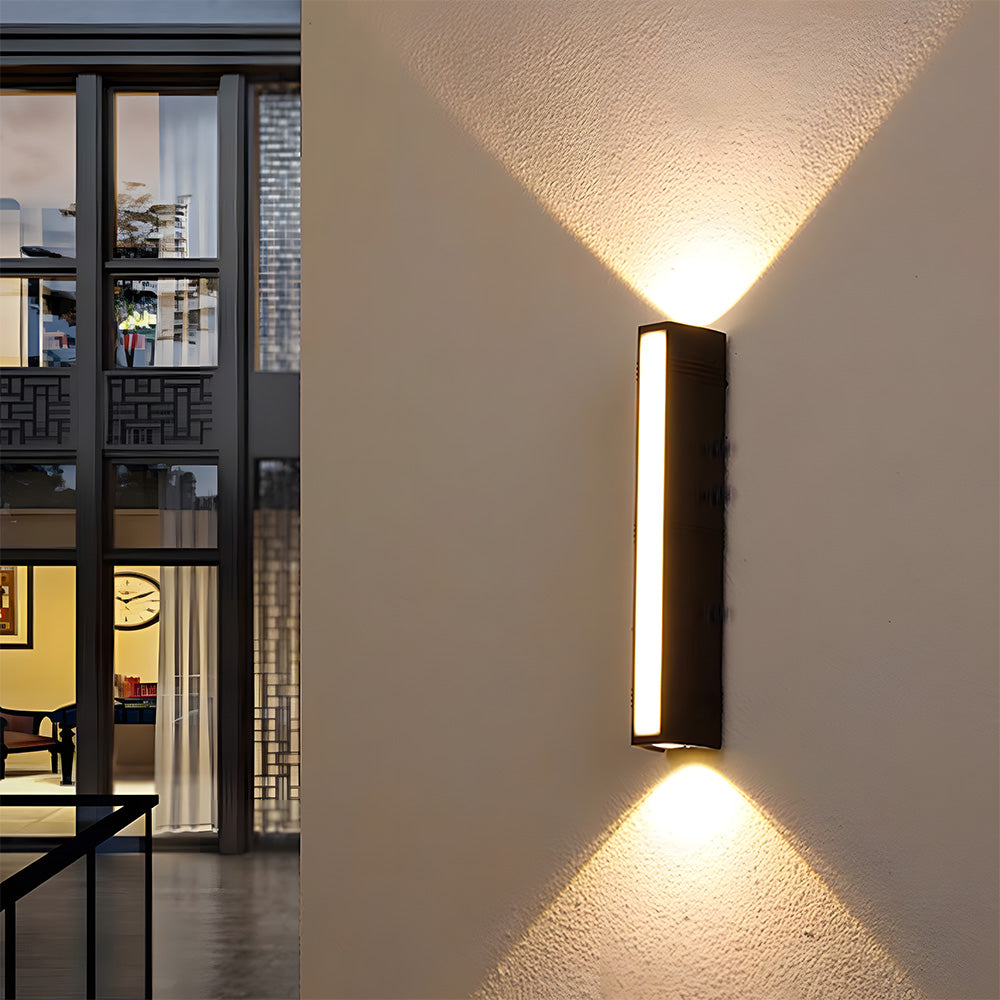 Modern black tube wall light installed on an architectural pillar casting a warm up and down glow