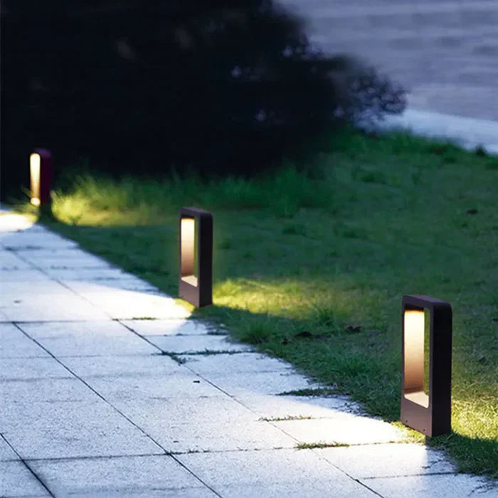 Modern black LED pathway bollard lights illuminating a paved residential walkway at dusk