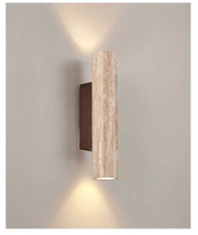 Modern cylindrical travertine wall sconce casting a warm up and down light on a plain wall