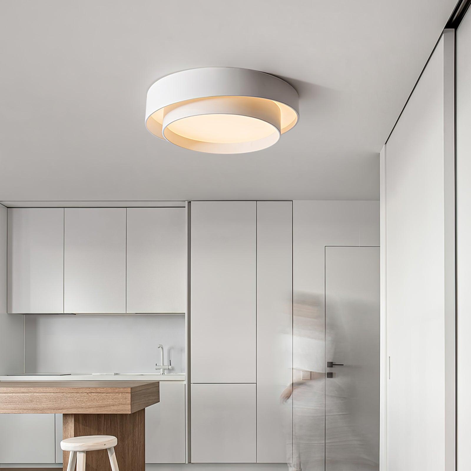 Modern white concentric ring ceiling light illuminating a bright, minimalist white kitchen space