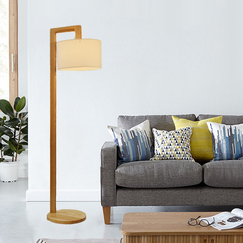 Modern wooden right-angle floor lamp with a beige fabric shade standing next to a living room sofa