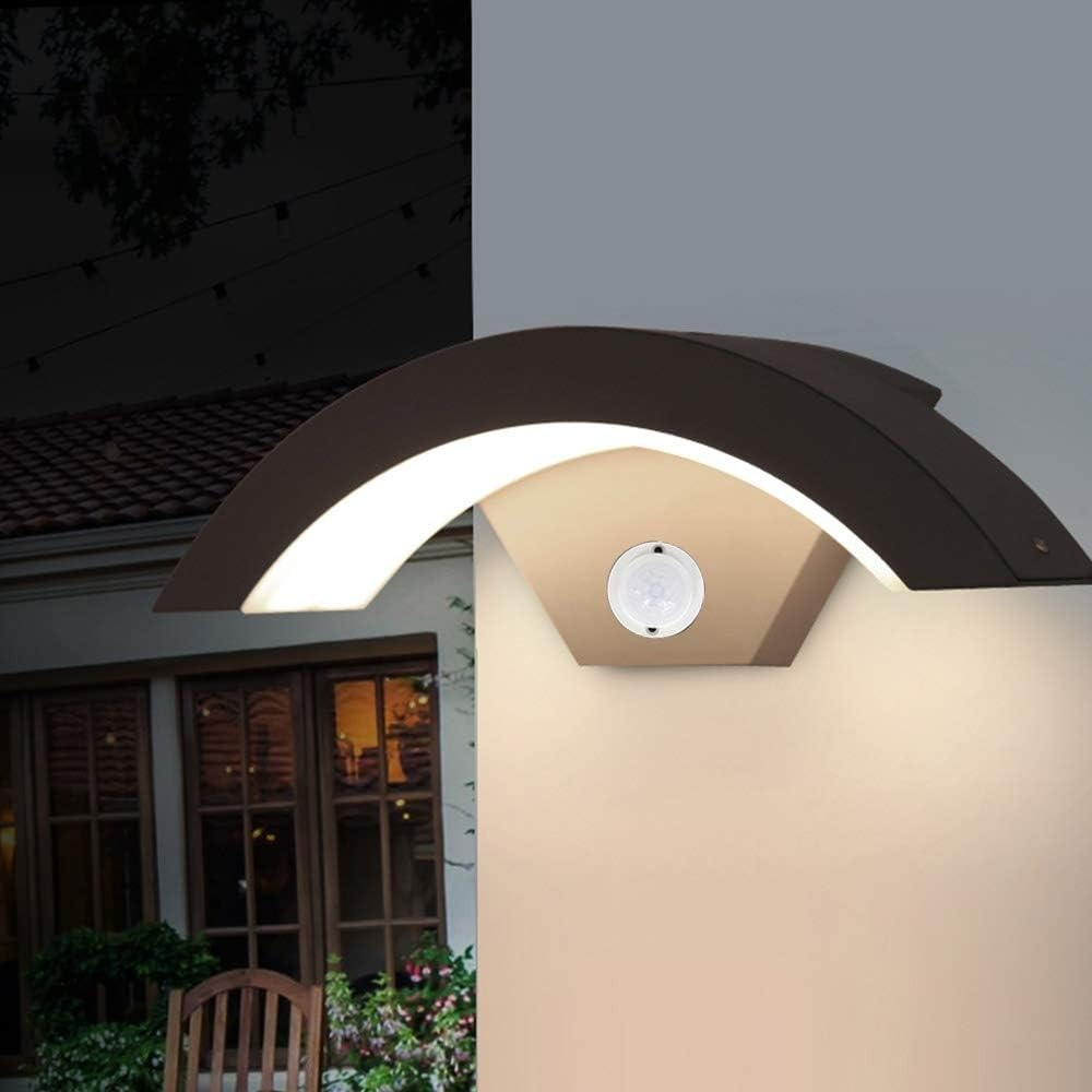 Close-up of the arched motion sensor porch light glowing warmly on an exterior wall at dusk