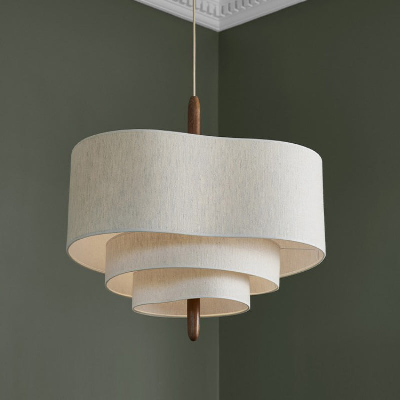 Close-up of the myska Japandi tiered linen pendant light with a wooden accent, glowing against a dark olive green wall