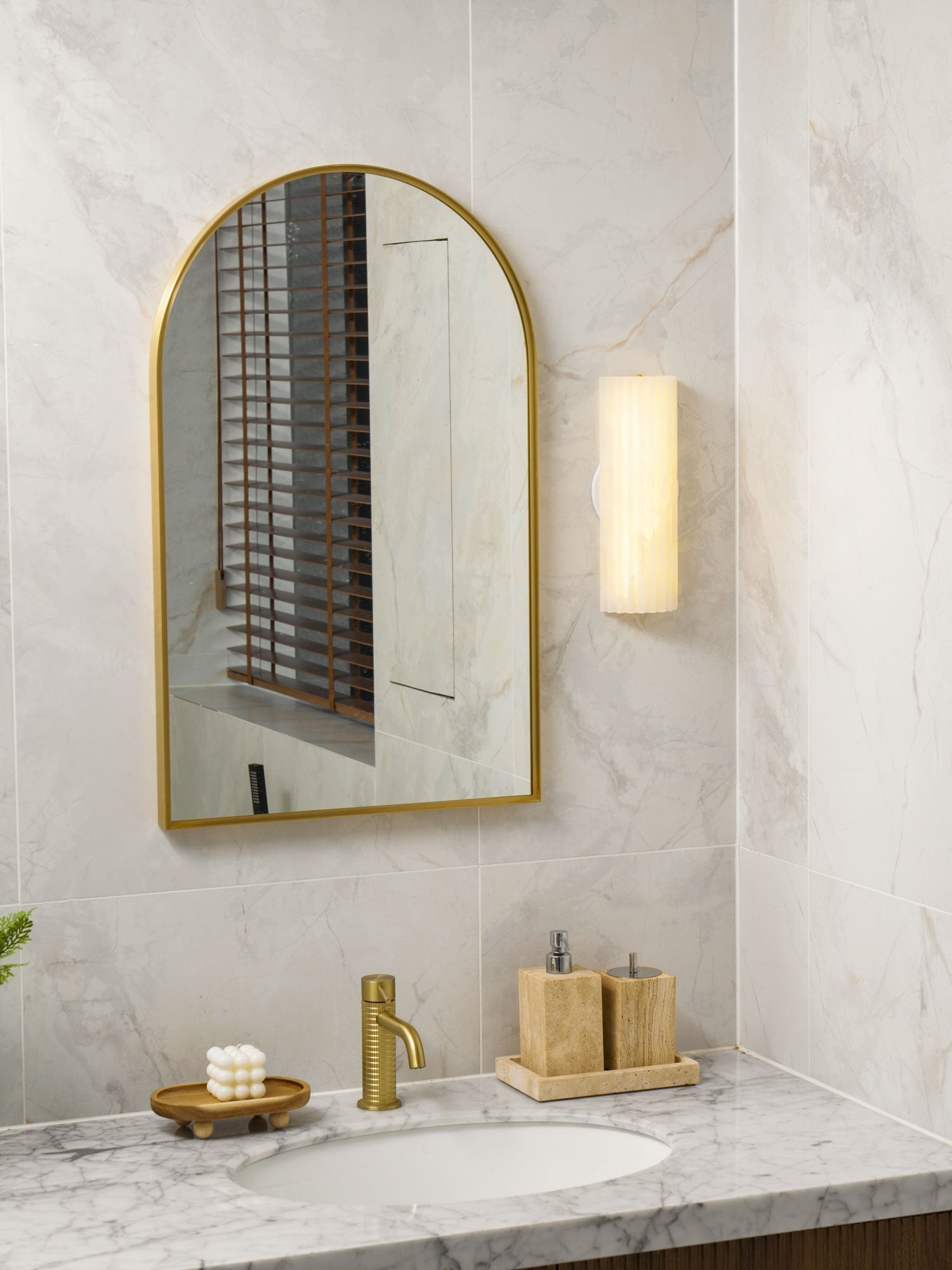 Natural alabaster wall sconce mounted beside a gold-framed bathroom mirror