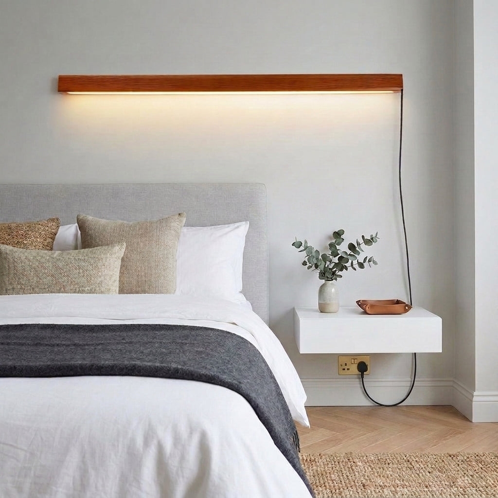 Nizku linear wood wall lamp above a bed with white and grey bedding and a floating nightstand with a plant