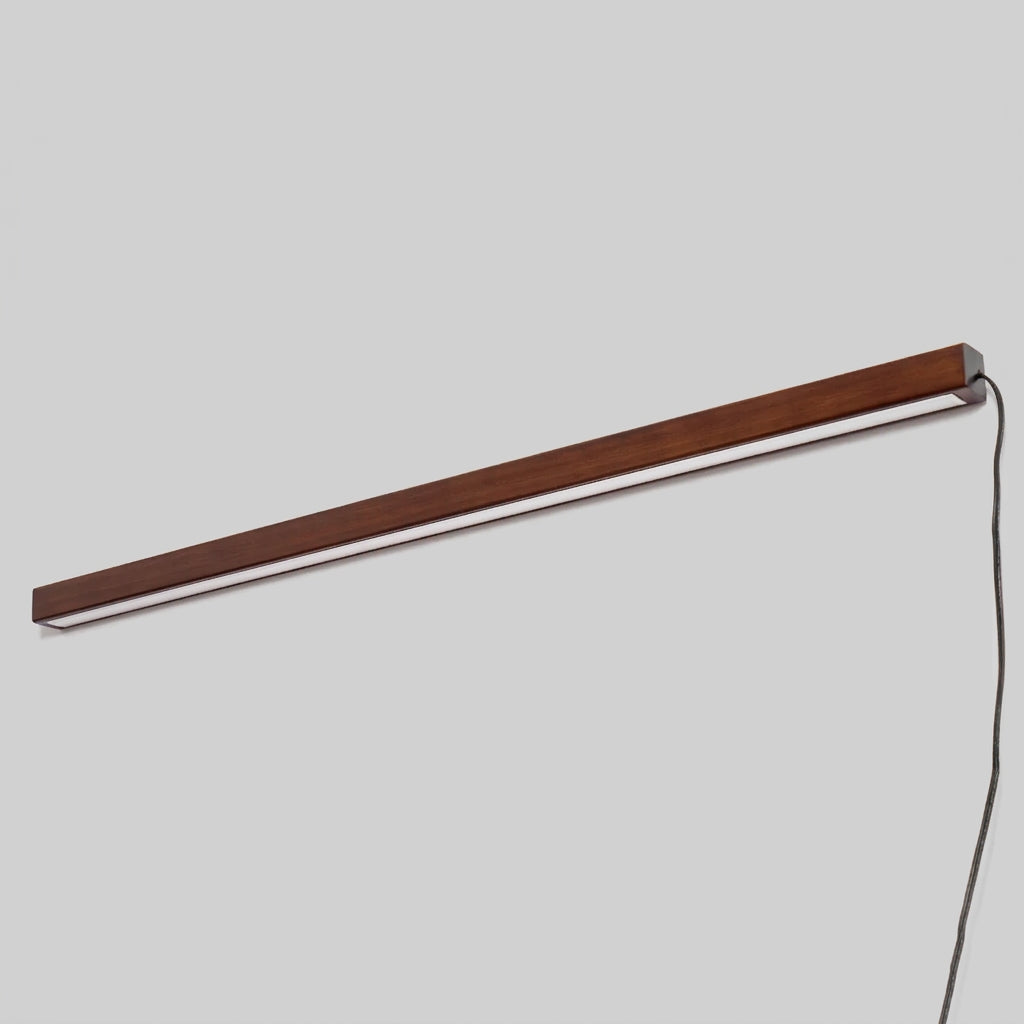 Full-length angled shot of the Nizku Walnut linear wall lamp with integrated LED strip lit