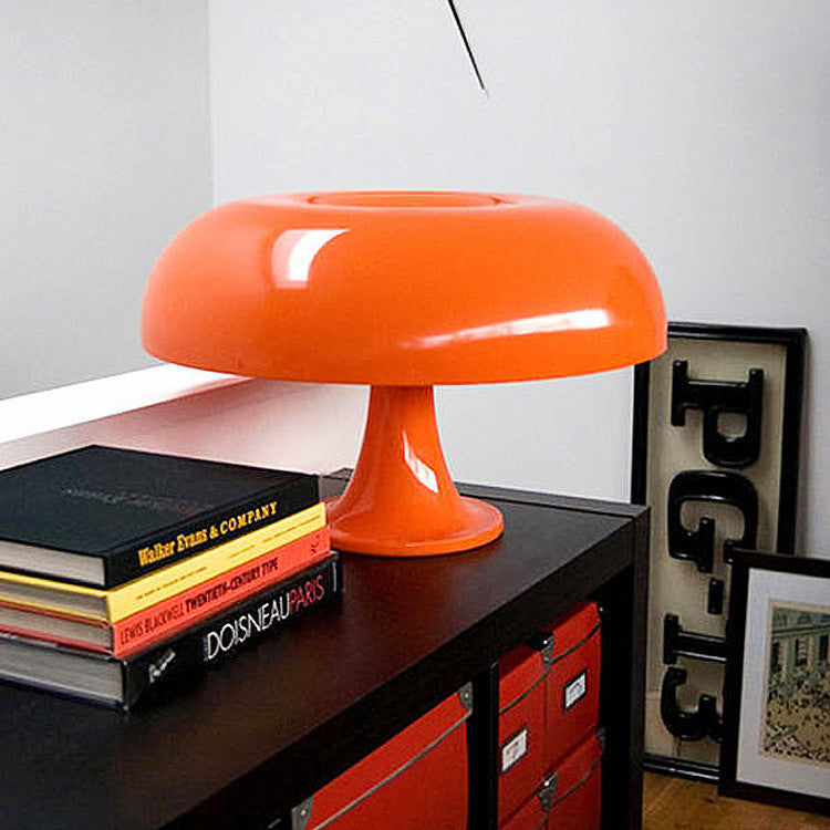 Orange 1970s style mushroom table lamp resting elegantly on a black cabinet with stacked books