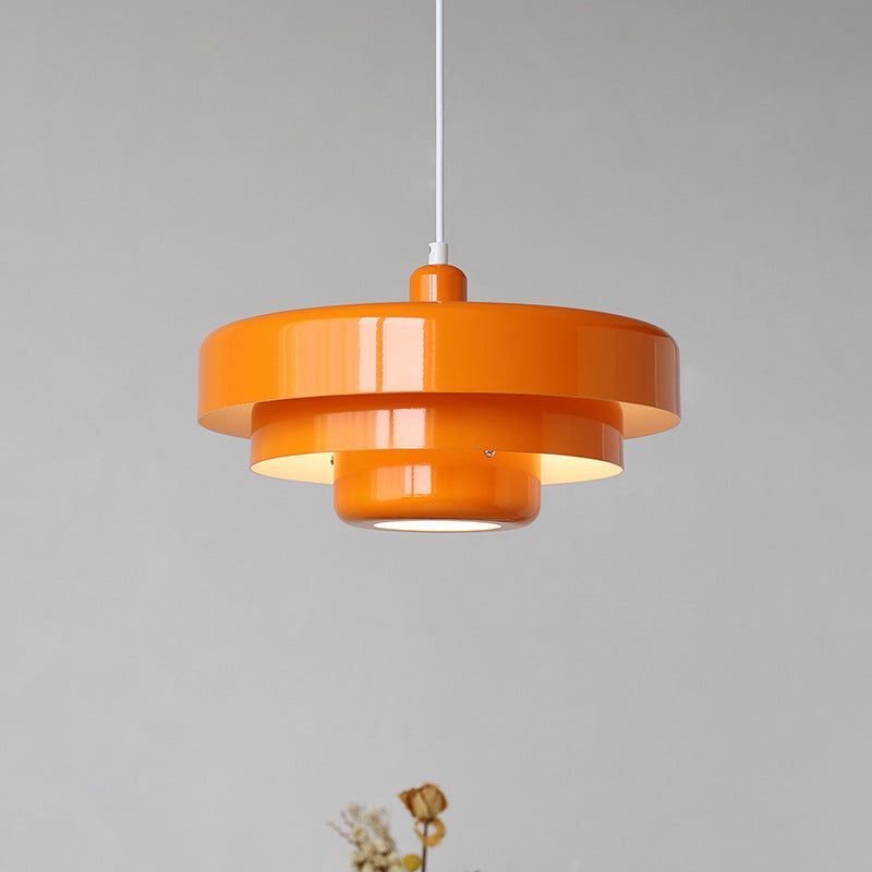 Bright orange mid-century modern layered pendant lamp isolated against a light grey background