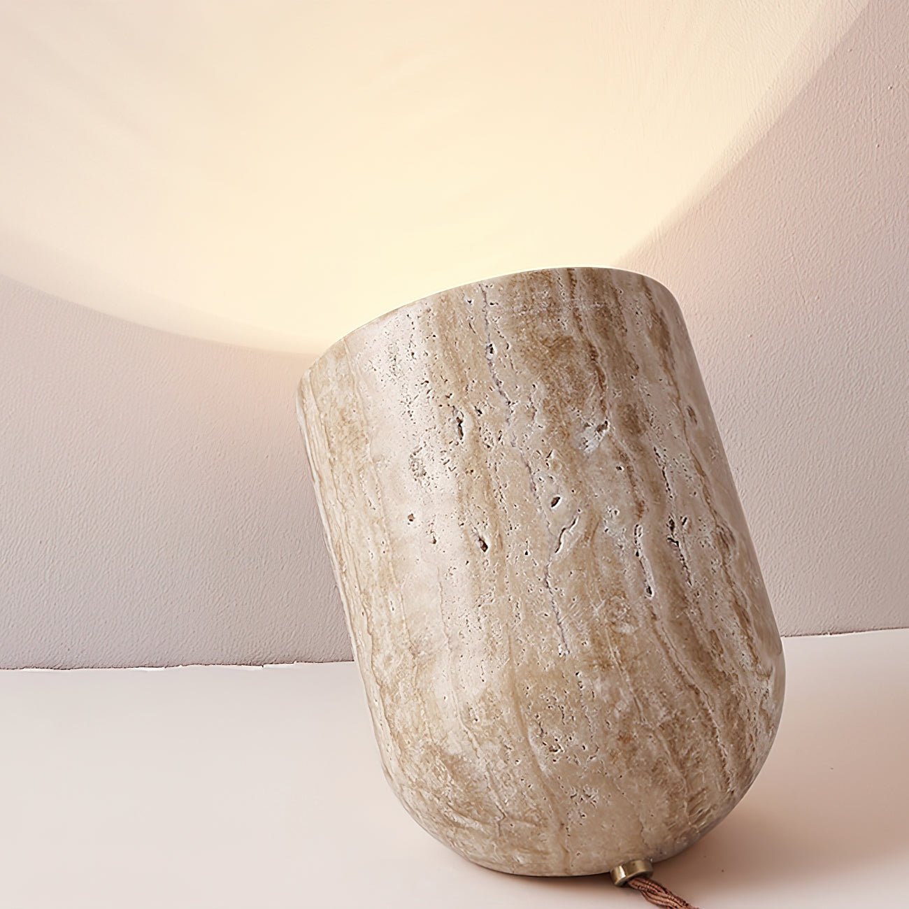 Organic stone bedside lamp carved from travertine, resting on a table and casting a soft upward light