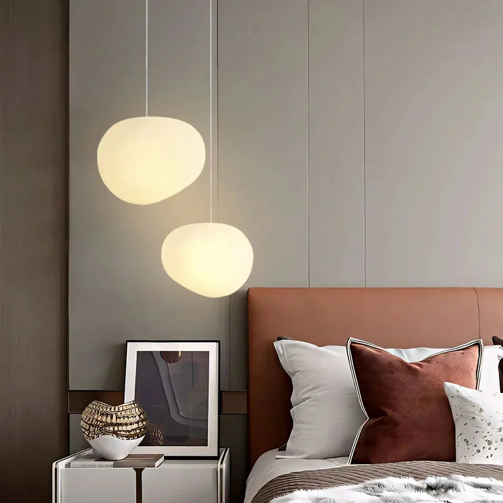 Pair of glowing glass stone pendant lights acting as warm bedside lighting in a modern bedroom