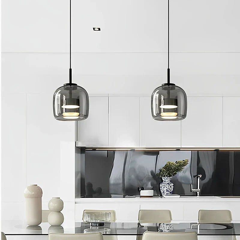 Pair of smoke grey glass pendant lights hanging above a bright, minimalist white kitchen counter