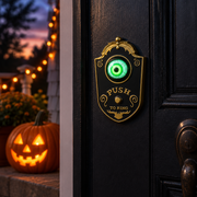 Peepbell black gothic eyeball doorbell mounted on a front door at dusk with a lit pumpkin on the porch
