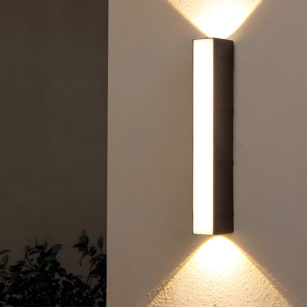 Close-up of a modern black up and down exterior peqi LED sconce glowing on a white wall