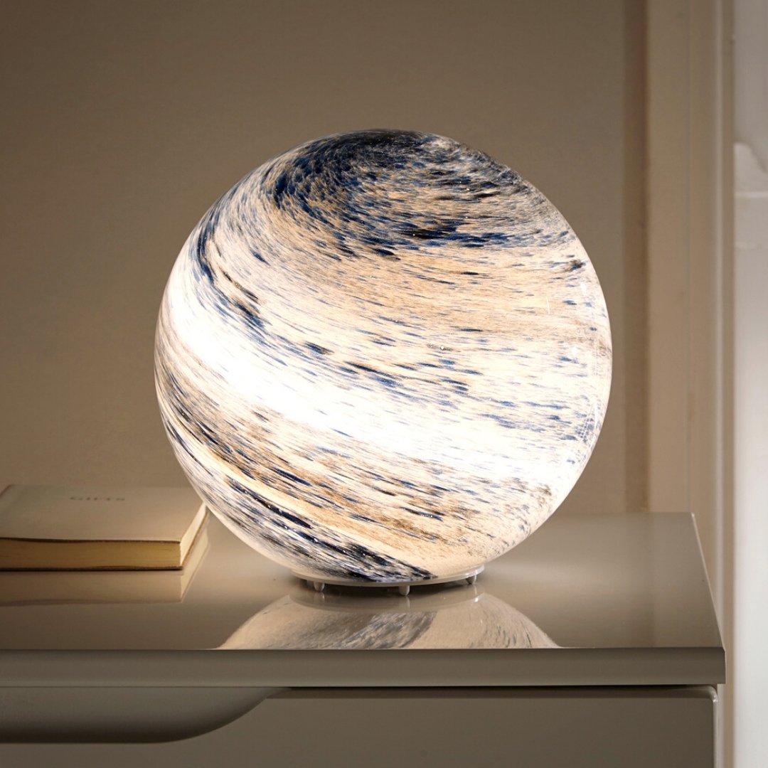 Modern planetary glass sphere pilo table lamp glowing warmly on a white bedside table next to a book