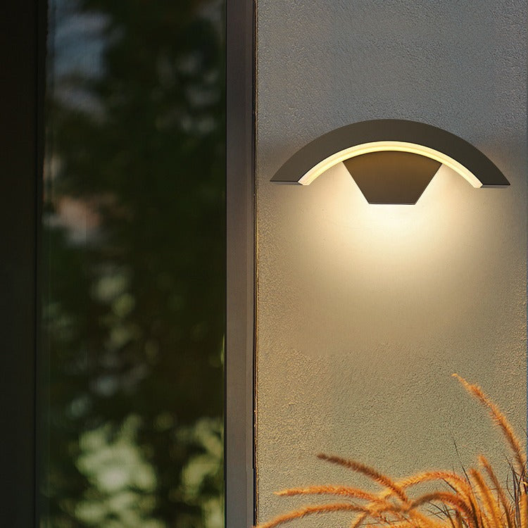 Black crescent exterior qaxo LED wall sconce casting warm light on a textured outdoor wall