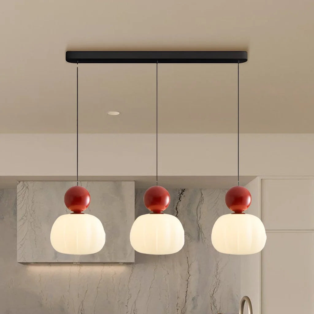 Red three-head linear kitchen island lighting adding a vibrant contrast to a neutral kitchen