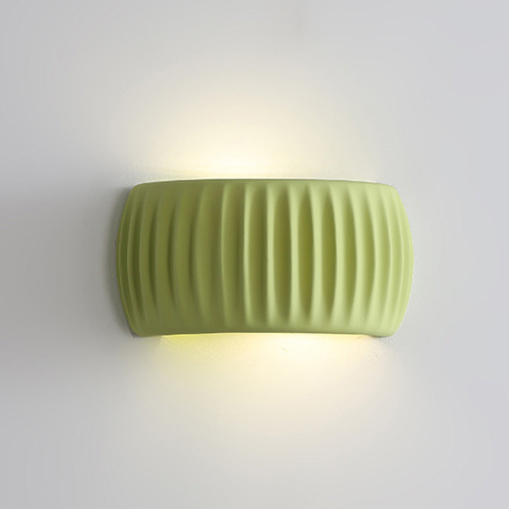 Close-up of a glowing ryfy green ribbed resin wall lamp casting up and down ambient light
