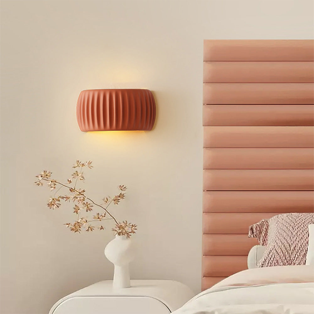 Warm ryfy orange fluted wall sconce mounted above a bedside table next to a pink velvet headboard