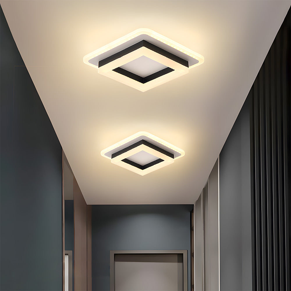 Pair of black square LED flush mount serq ceiling lights casting a warm glow in a dark minimalist corridor