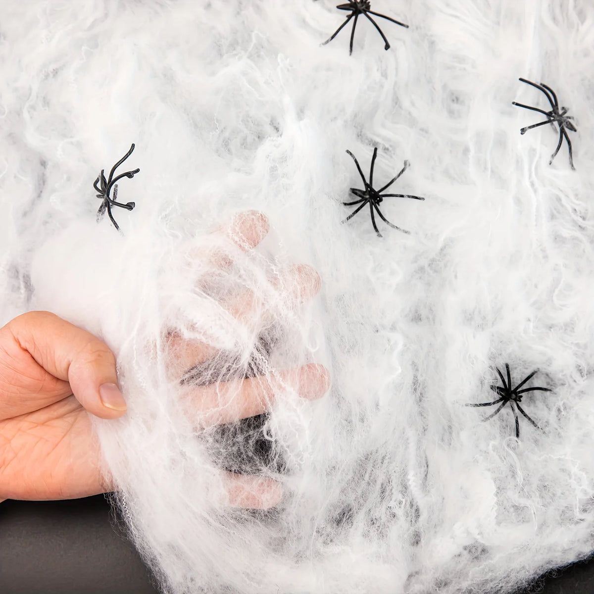 Hand pulling apart the Silkshroud stretch cobweb fibres to show the fine texture with spiders
