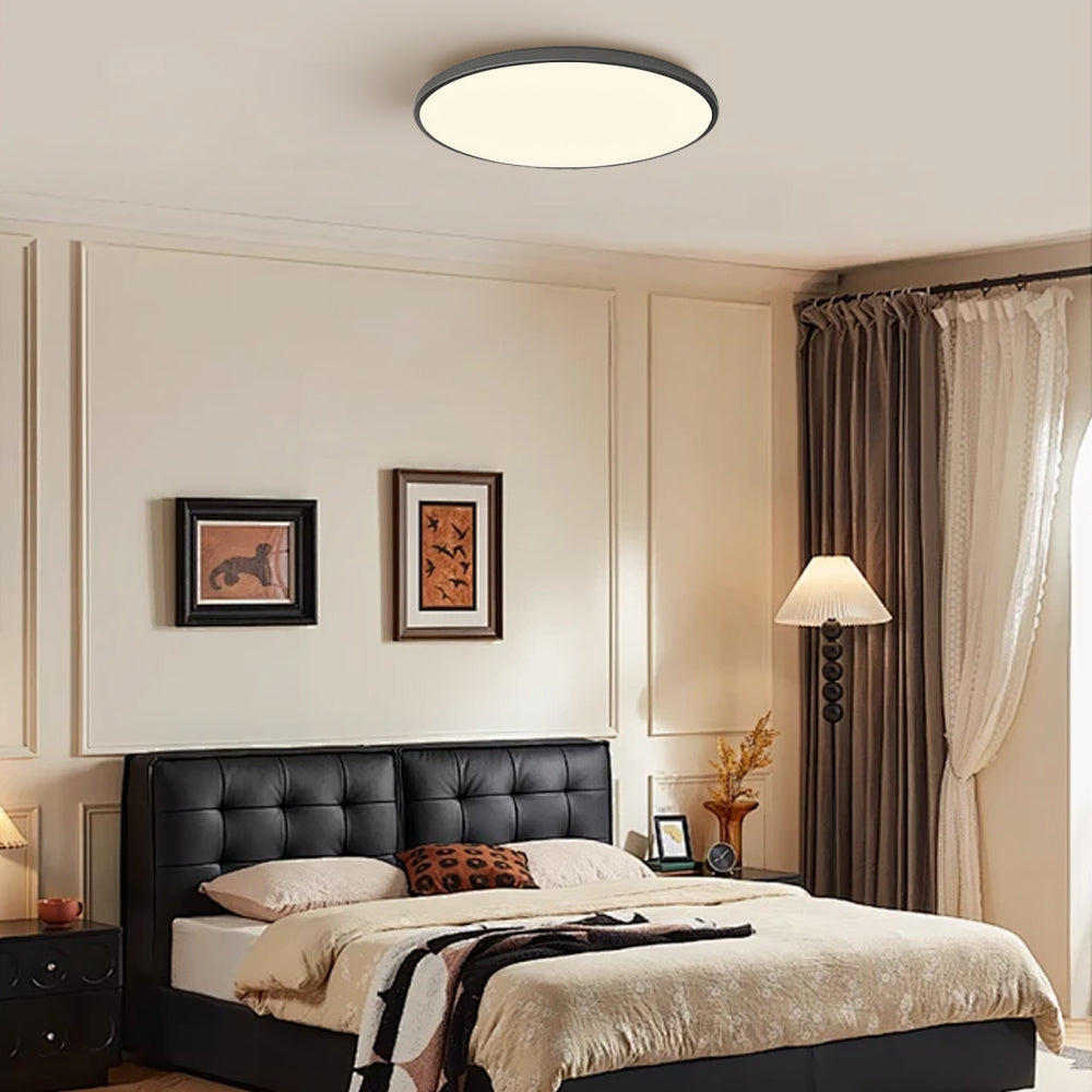 Silver round LED ceiling light installed above a bed with a black headboard in a modern room