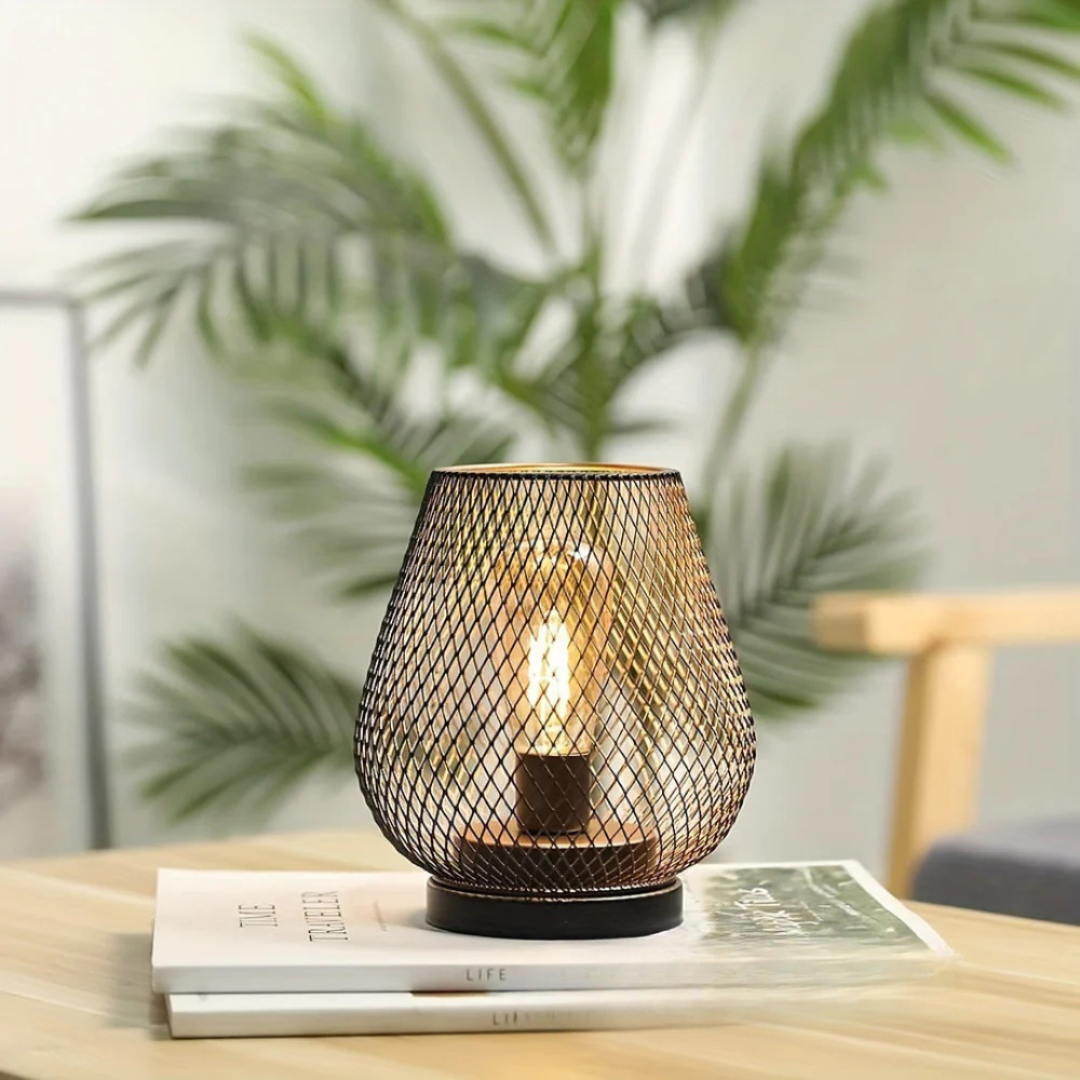 Single portable industrial LED table lamp resting on a wooden side table in a bright, modern room with plants