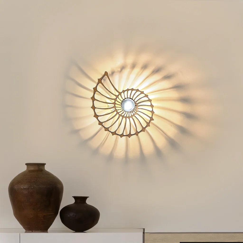 Small luxurious gold Nautilus shell wall sconce glowing warmly against a plain wall with rustic vases