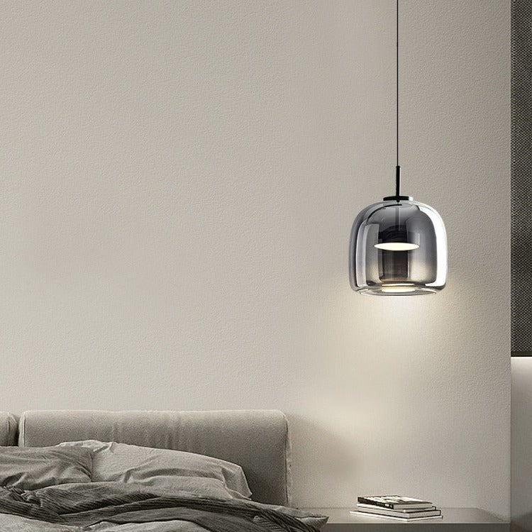 Smoke grey glass pendant light casting a soft, moody glow next to a modern bed