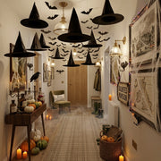 Multiple Spookcap black witch hats hung from the ceiling of a British Halloween-decorated hallway with hanging bats