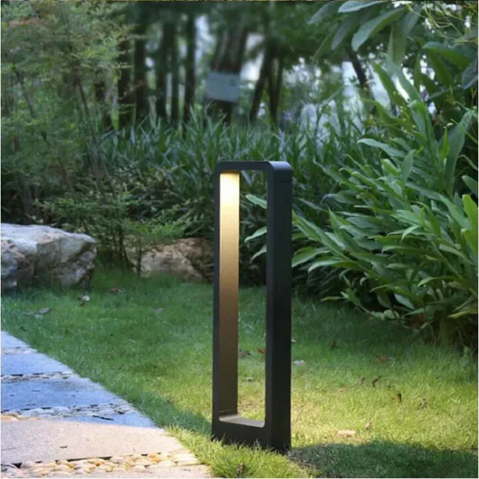 Tall black rectangular LED garden bollard light installed on a lush green lawn