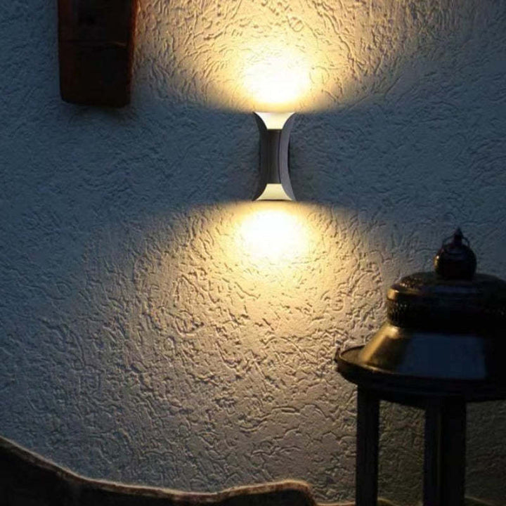 Waterproof hourglass teka sconce illuminating a textured outdoor patio wall at night