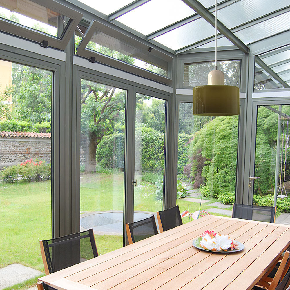 Green mid-century modern tepa glass pendant lights suspended in a bright, airy conservatory dining room