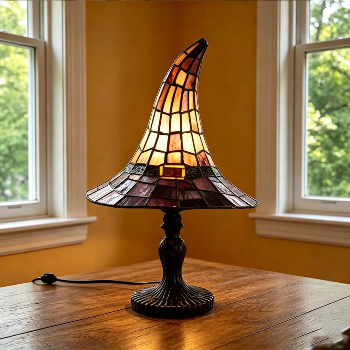 Tiffspell witch hat table lamp lit on a wooden table in front of a window