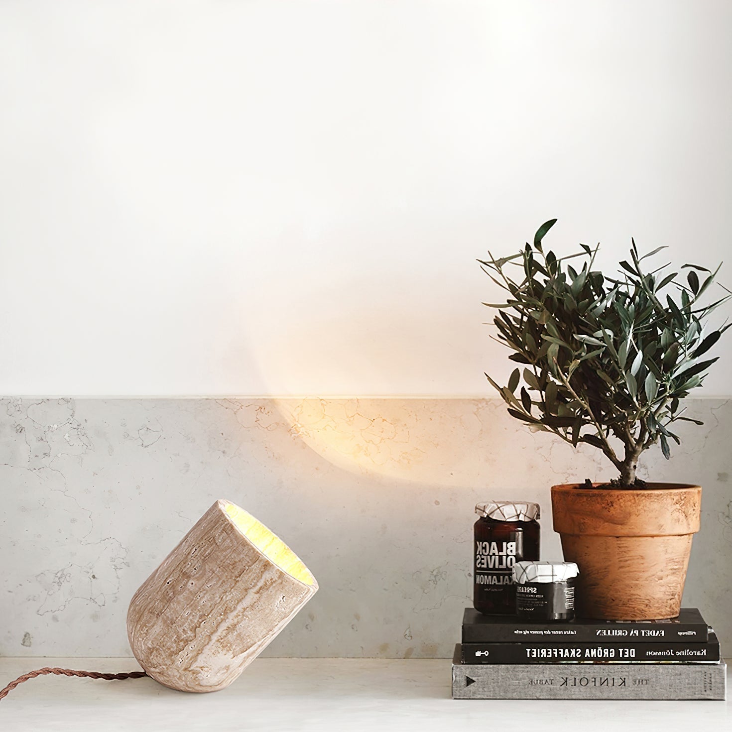 Natural travertine table lamp styled on a surface next to books and a small potted plant in a modern home