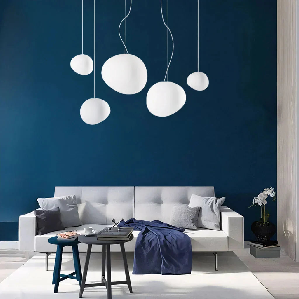 Cluster of multiple tupel glass pebble pendant lights against a dark blue living room accent wall