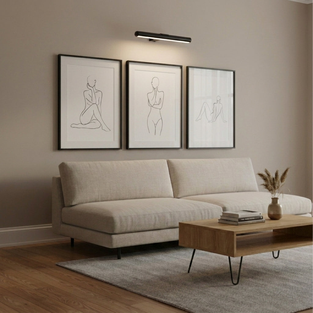 Black Tuvqi picture light above a three-piece gallery wall in a living room