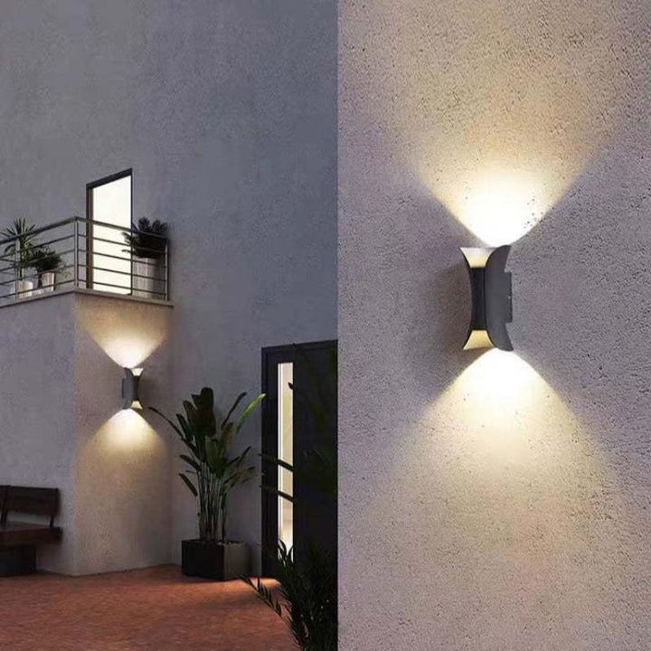 Pair of modern hourglass outdoor wall lights illuminating a contemporary home facade in the evening