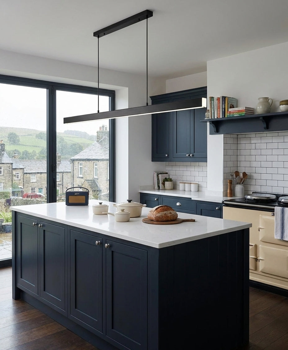Uvza linear pendant light hanging above a kitchen island with navy cabinets and open shelving