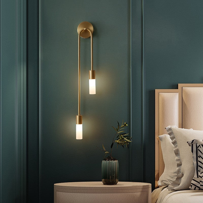 Gold dual-light vergs wall sconce casting a warm ambient glow in a moody, dark green bedroom