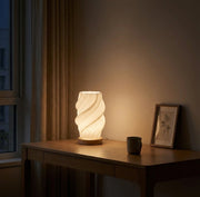 Volzi cream 3D wave table lamp on a wooden desk beside a window