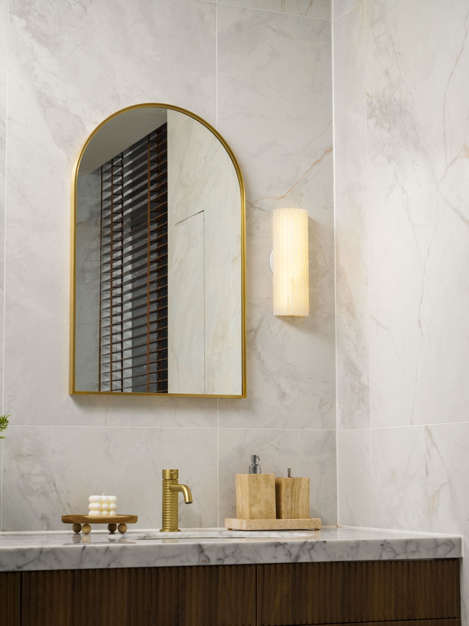 Warm LED alabaster sconce casting a soft glow over a bathroom sink and wooden accessories