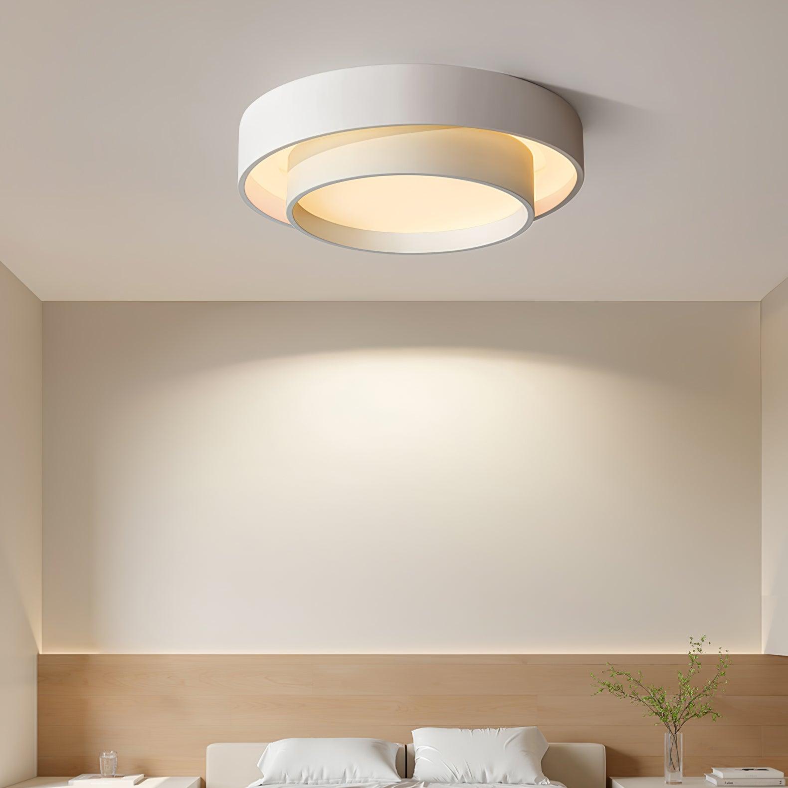 White double-ring LED flush mount fixture casting a warm ambient glow above a modern bed