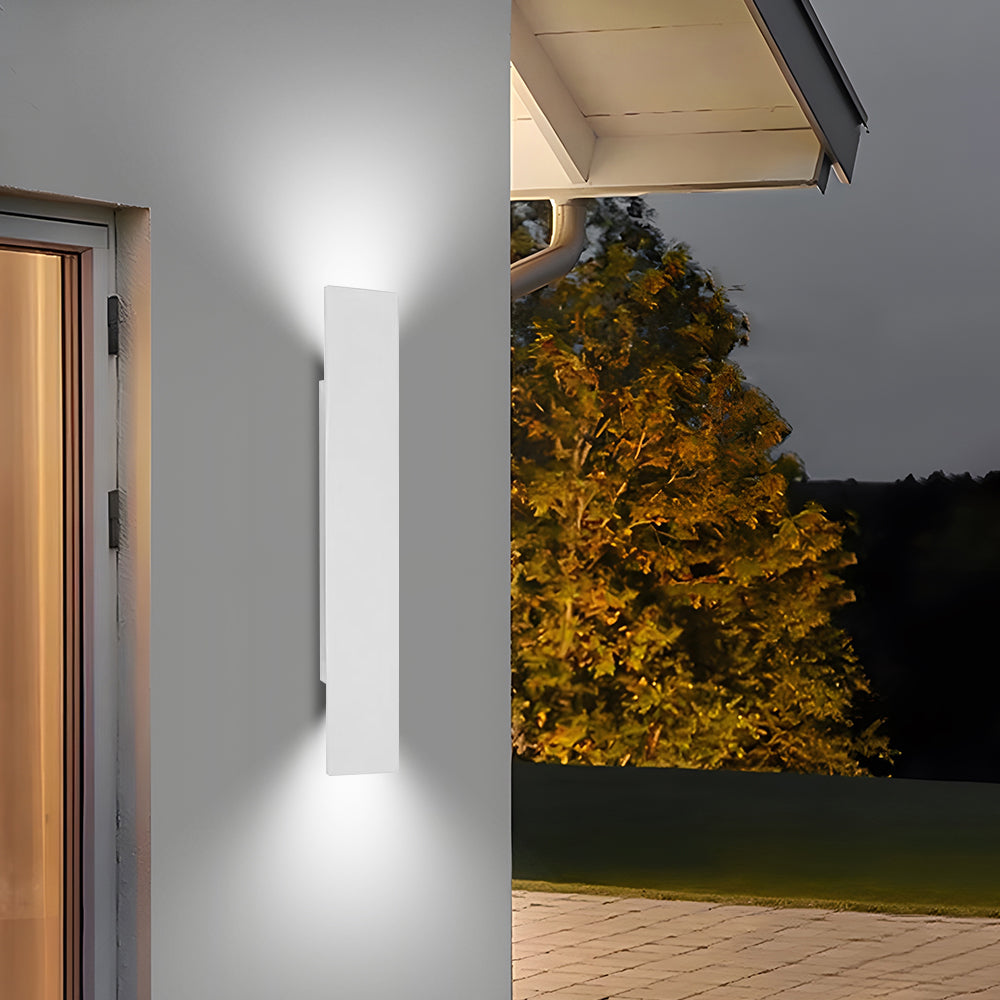 White exterior up and down wall sconce glowing warmly against a light wall