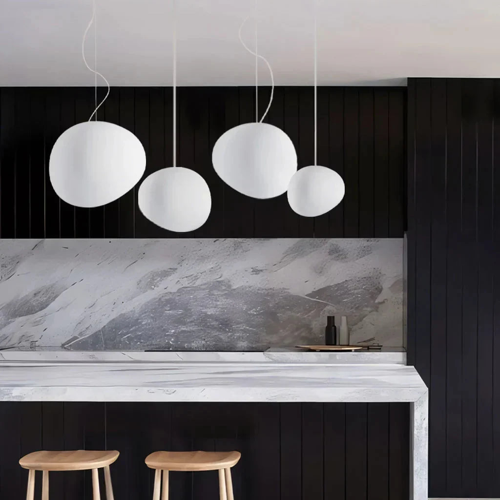 Three white glass stone pendant lights illuminating a sleek modern kitchen island