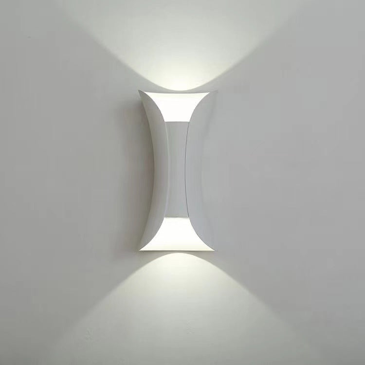 Sleek white modern hourglass LED wall sconce glowing crisply on a light wall