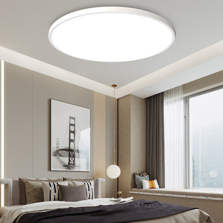 Modern white round LED flush mount ceiling light illuminating a contemporary bedroom space