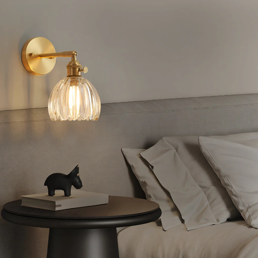 Clear glass xetyl lotus wall lamp acting as an elegant reading light next to a minimalist grey bed