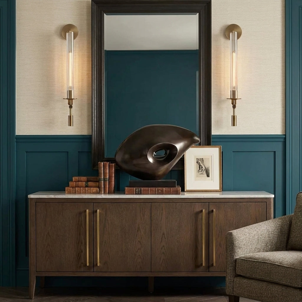 A pair of Xilpo wall sconces flanking a mirror above a wooden sideboard styled with a bronze sculpture and books