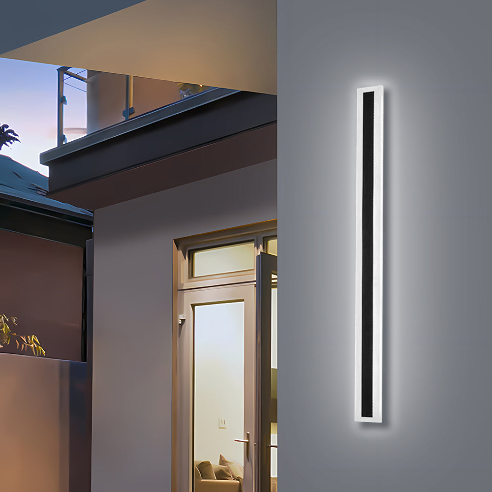 Angled view of a glowing xura black linear outdoor LED sconce mounted next to a glass door