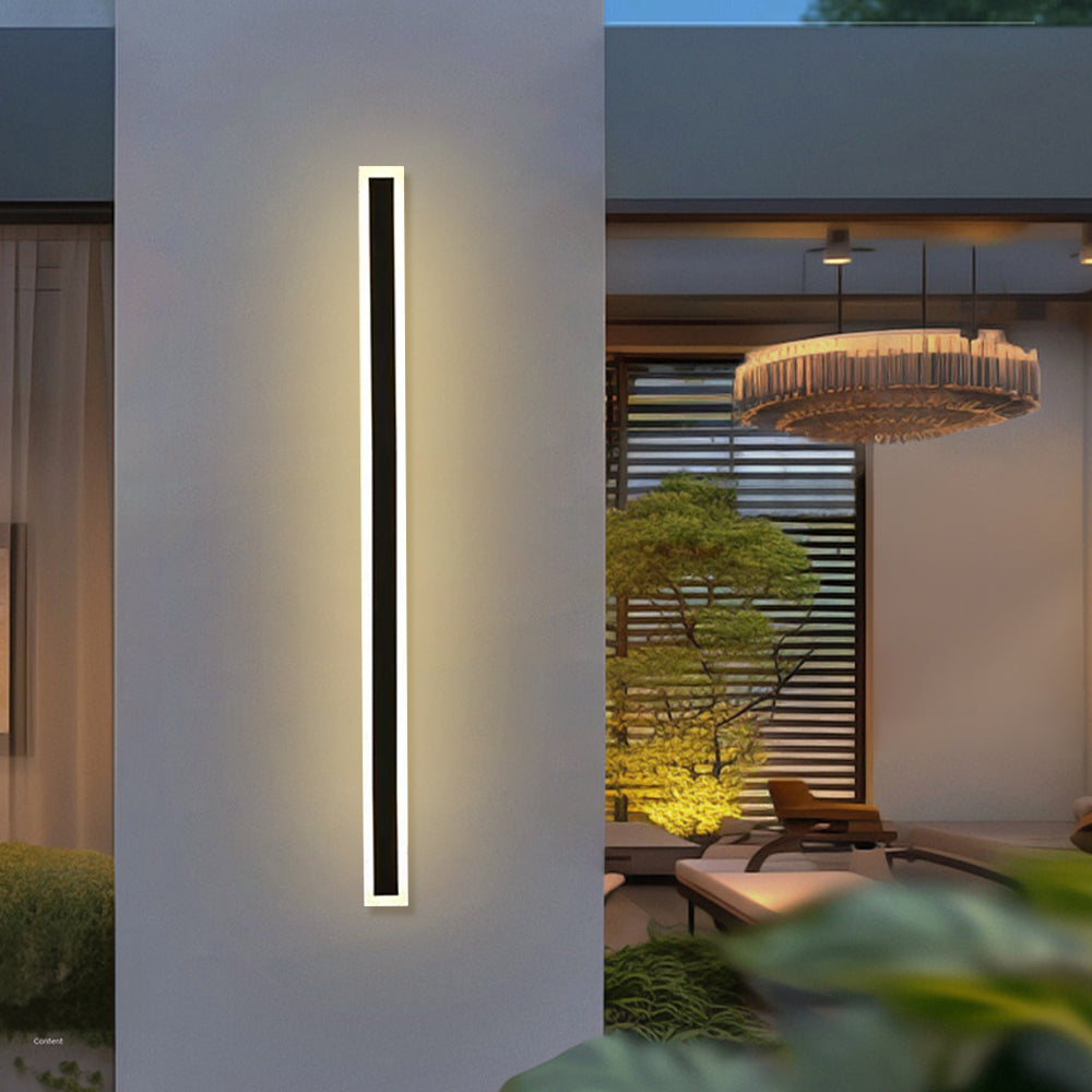 Single long black xura linear wall lamp mounted on a modern covered patio pillar